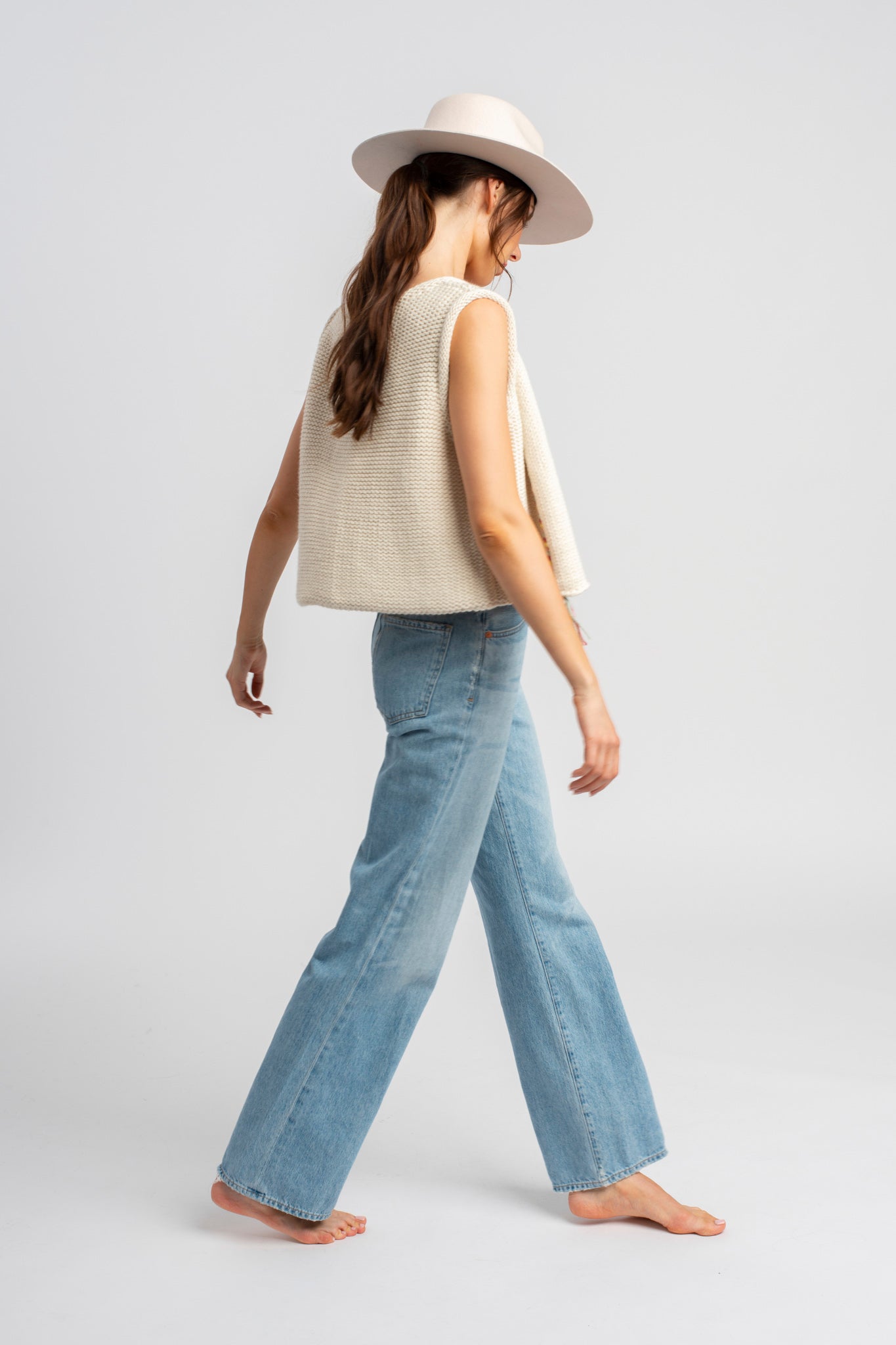Model wearing white sweater knit vest in alpaca wool, standing outside, side view walking
