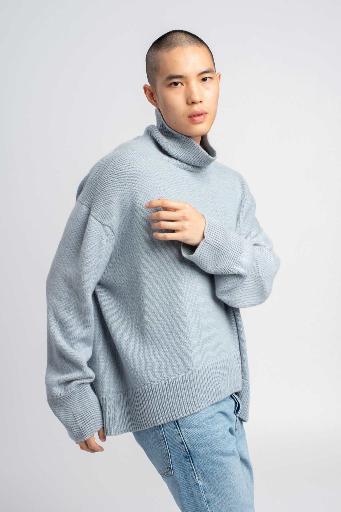 Model wearing turtleneck oversized sweater in blue alpaca wool, arm across