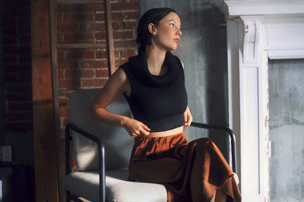 Model wearing black sweater crop top in alpaca wool, beside fireplace