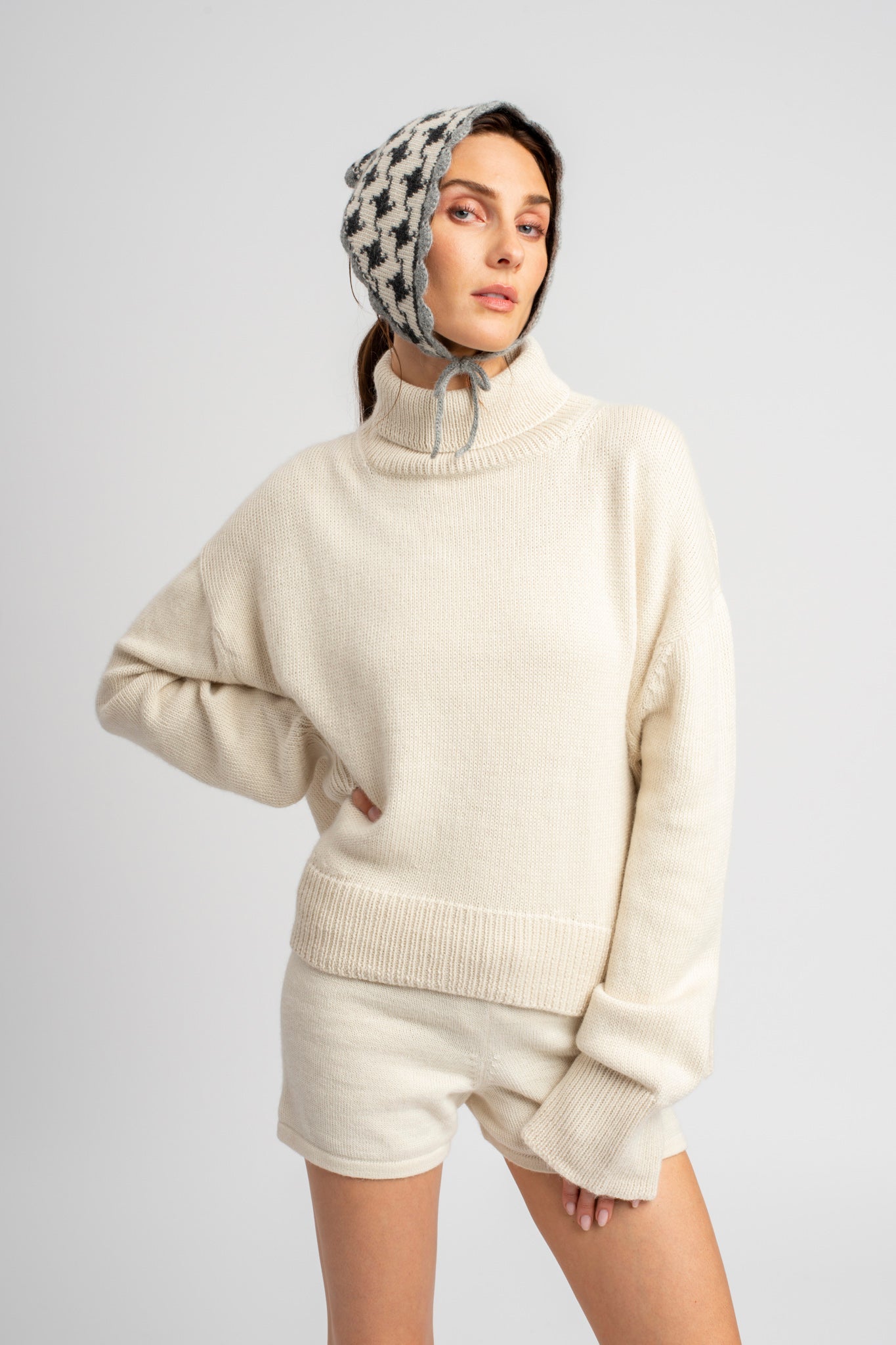 Model wearing knitwear alpaca wool headscarf in white & grey reversible houndstooth & white sweater, standing
