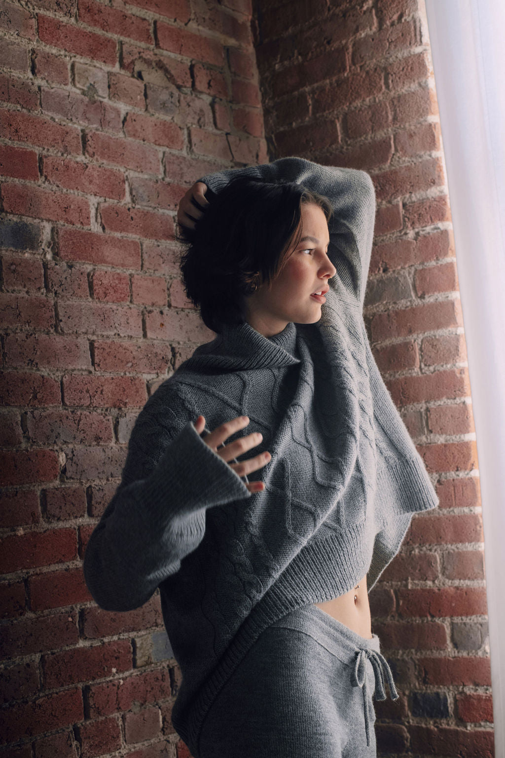 Model wearing oversized cable sweater in light grey alpaca wool, standing
