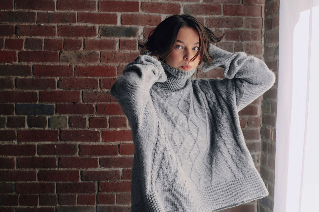 Model wearing oversized cable sweater in light grey alpaca wool, front view