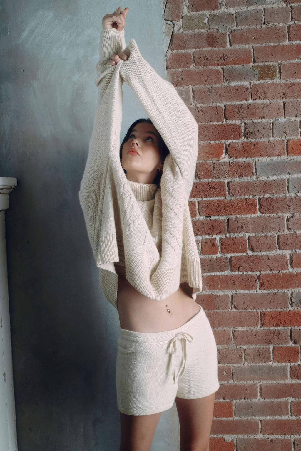 Model wearing oversized cable sweater in white alpaca wool, arms up