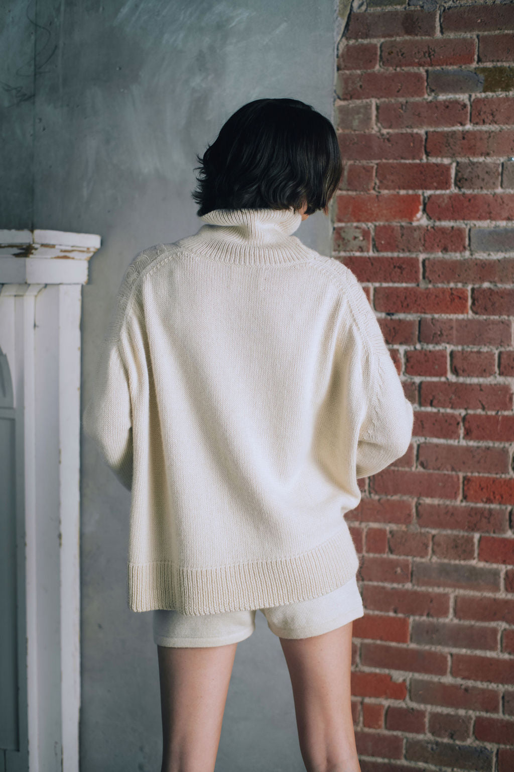 Model wearing oversized cable sweater in white alpaca wool, back