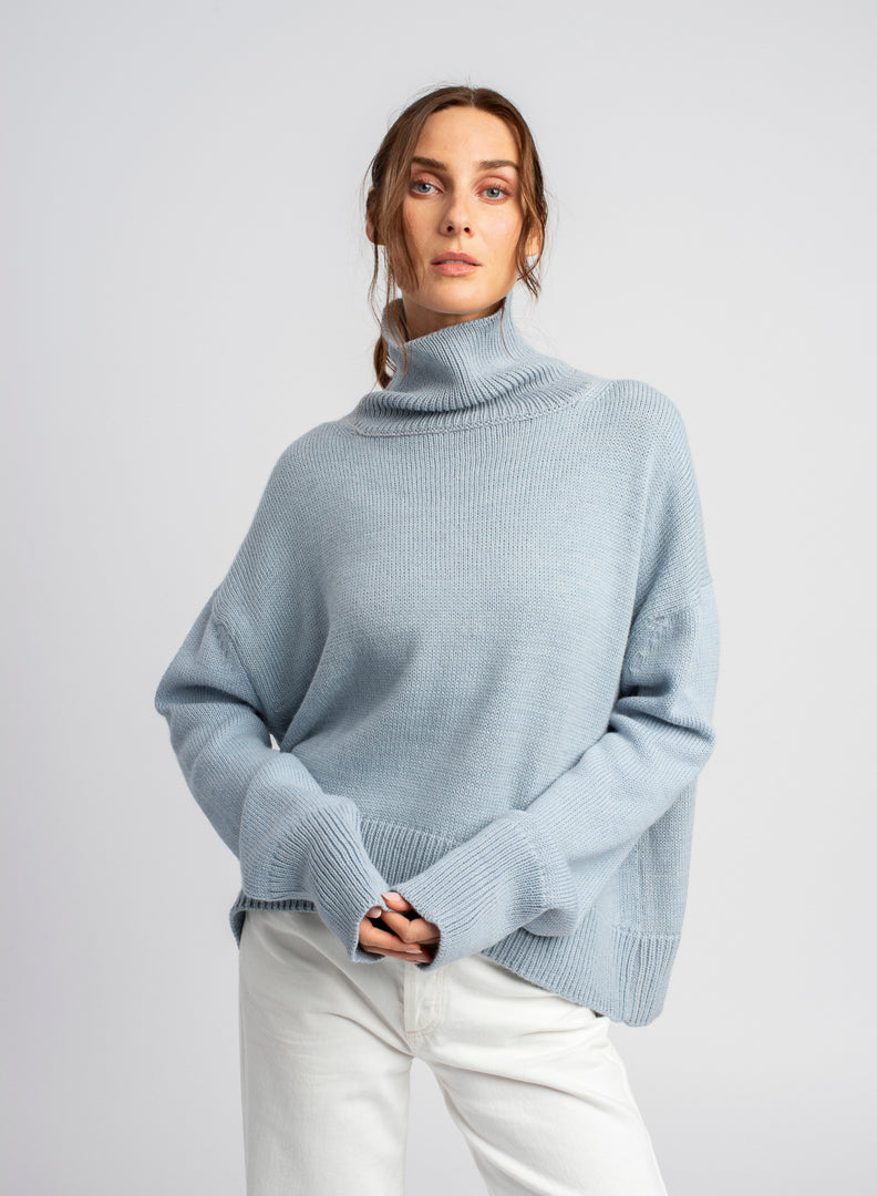 Model wearing turtleneck oversized sweater in blue alpaca wool, front view