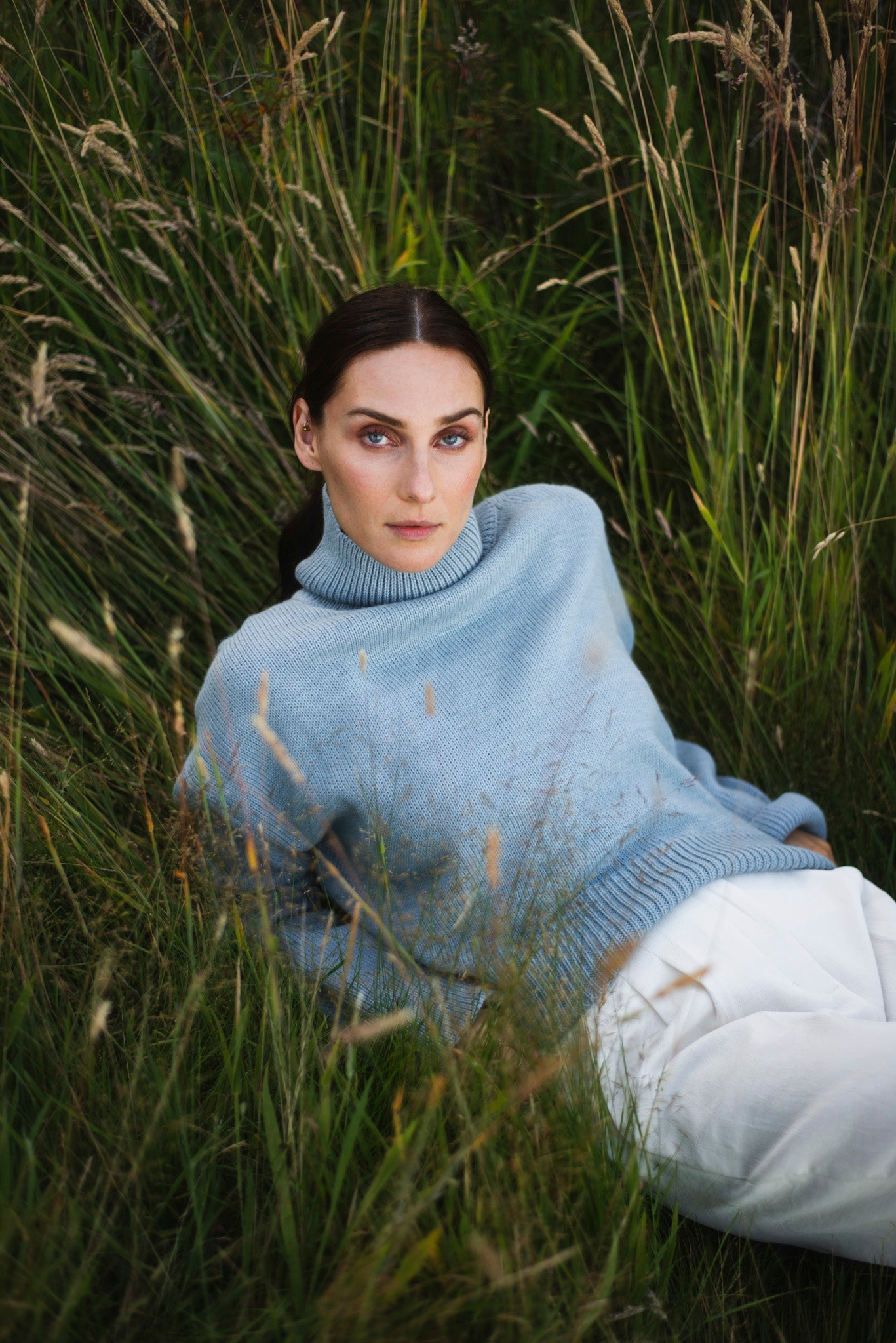 Model wearing turtleneck oversized sweater in blue alpaca wool, reclined