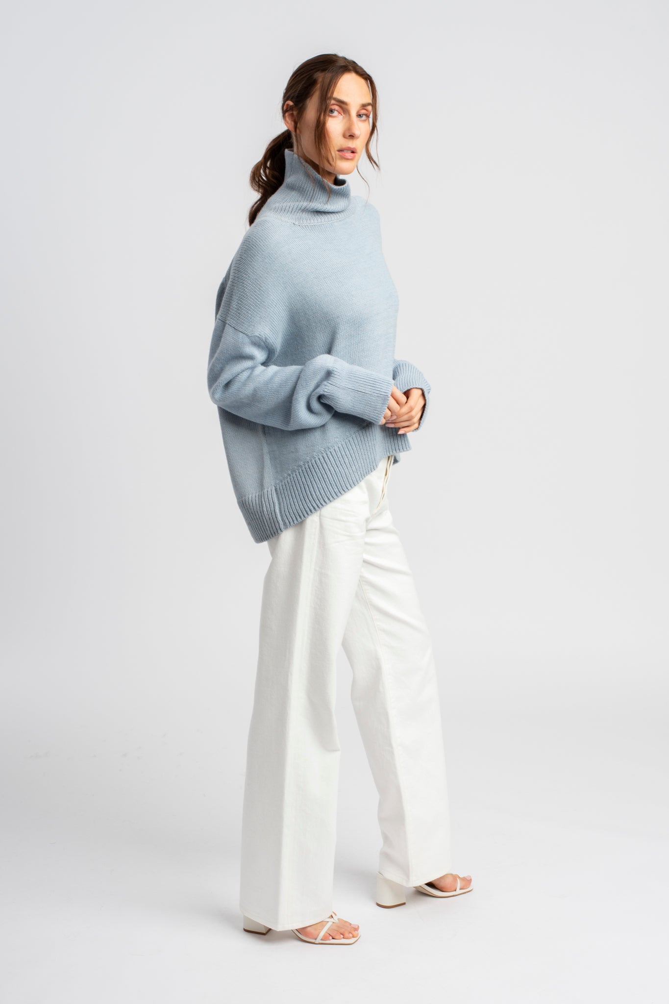 Model wearing turtleneck oversized sweater in blue alpaca wool, side distance