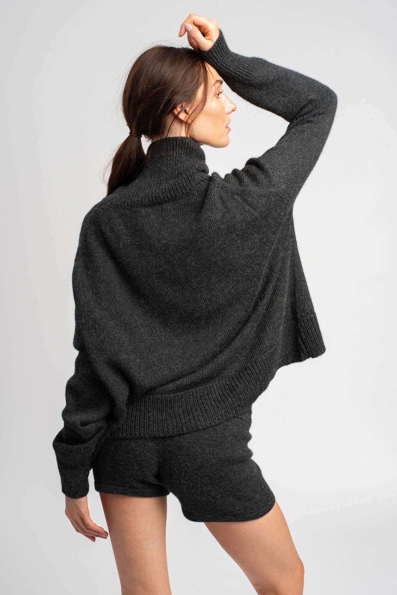 Model wearing turtleneck oversized sweater in dark grey alpaca wool, back arm up
