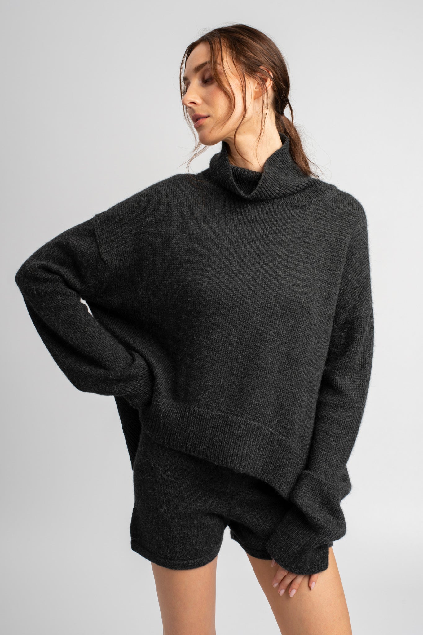 Model wearing turtleneck oversized sweater in dark grey alpaca wool, hand on hip
