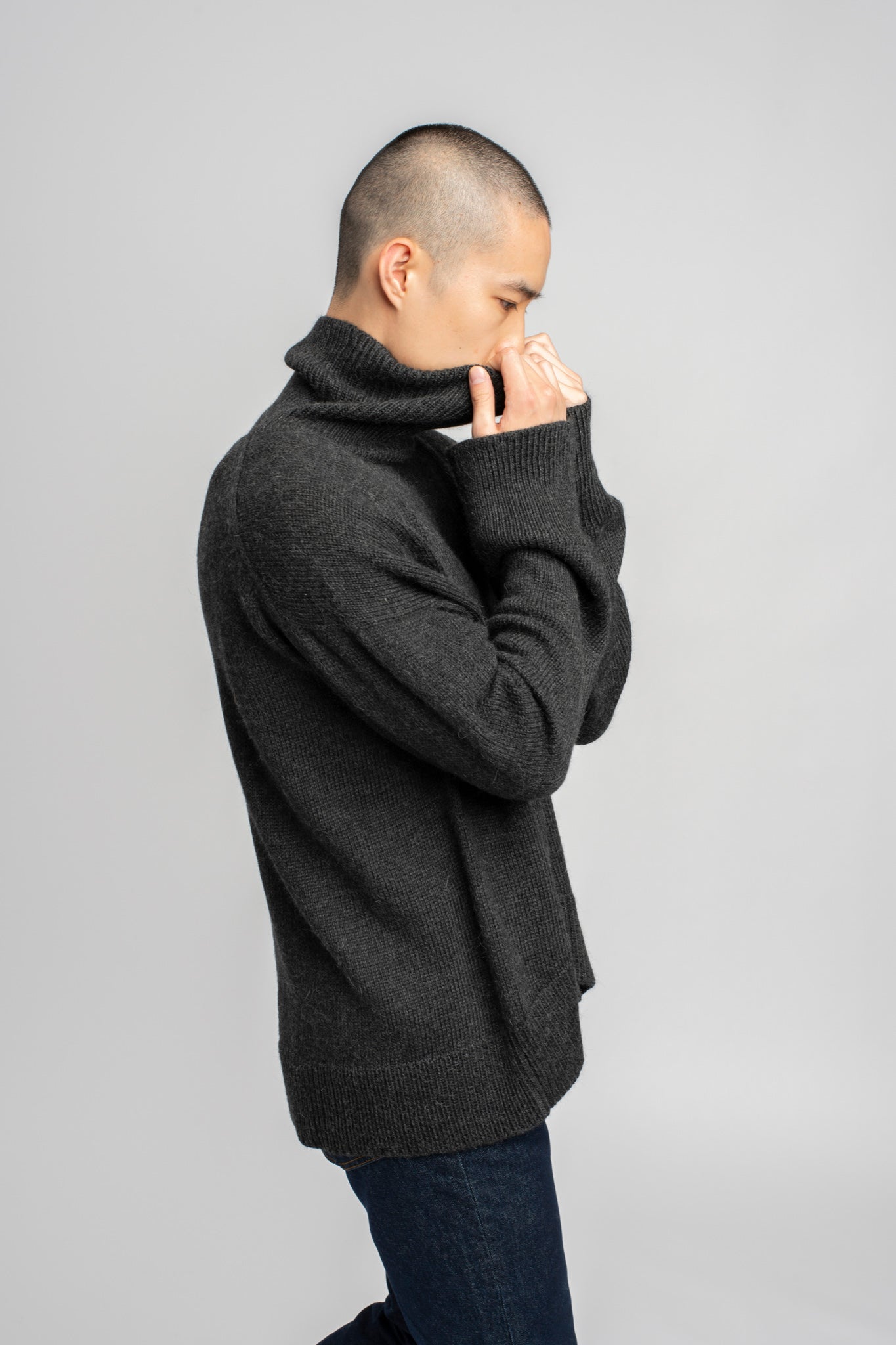 Model wearing turtleneck oversized sweater in dark grey alpaca wool, side arms up