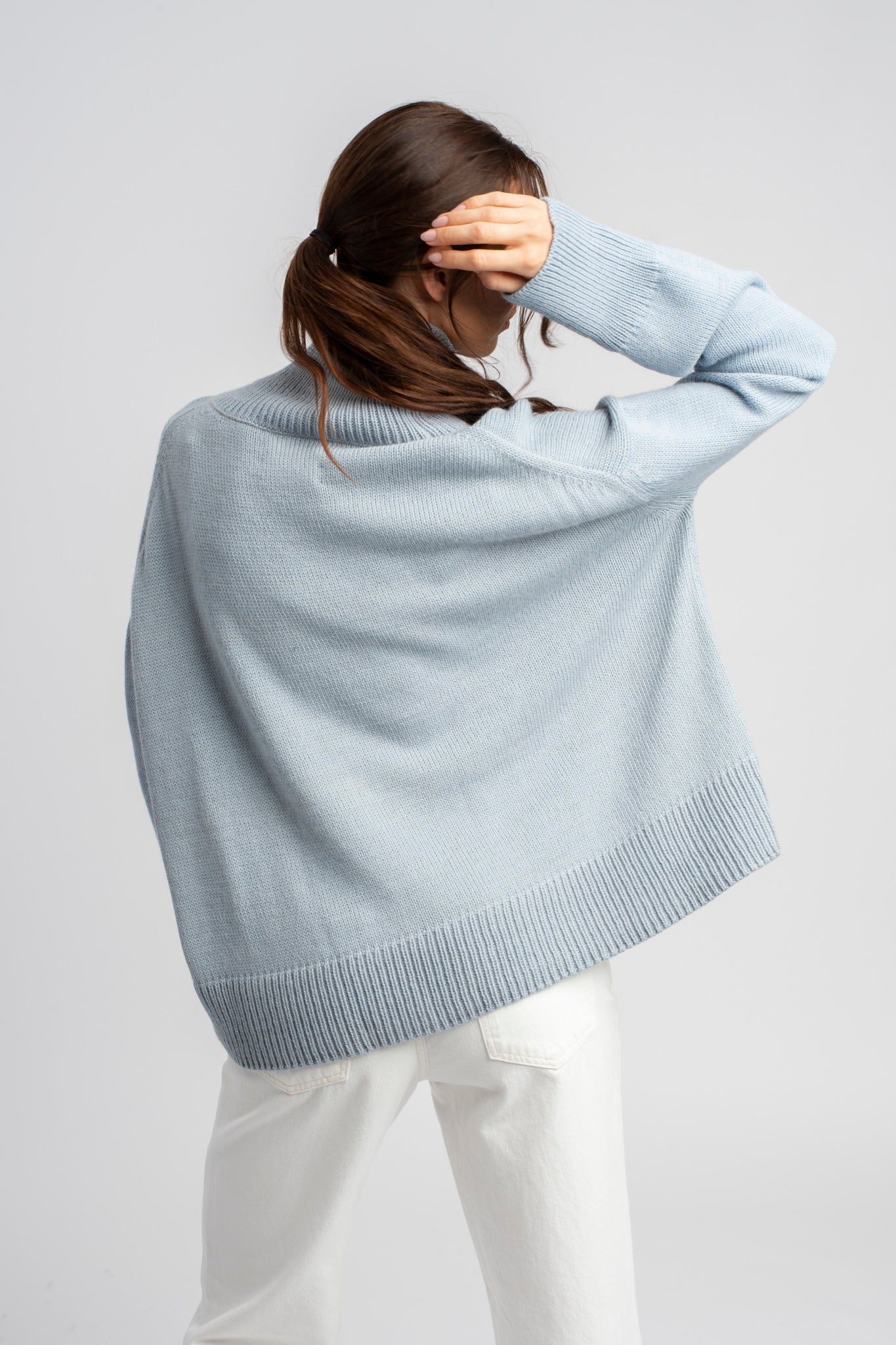 Model wearing turtleneck oversized sweater in blue alpaca wool, back view standing