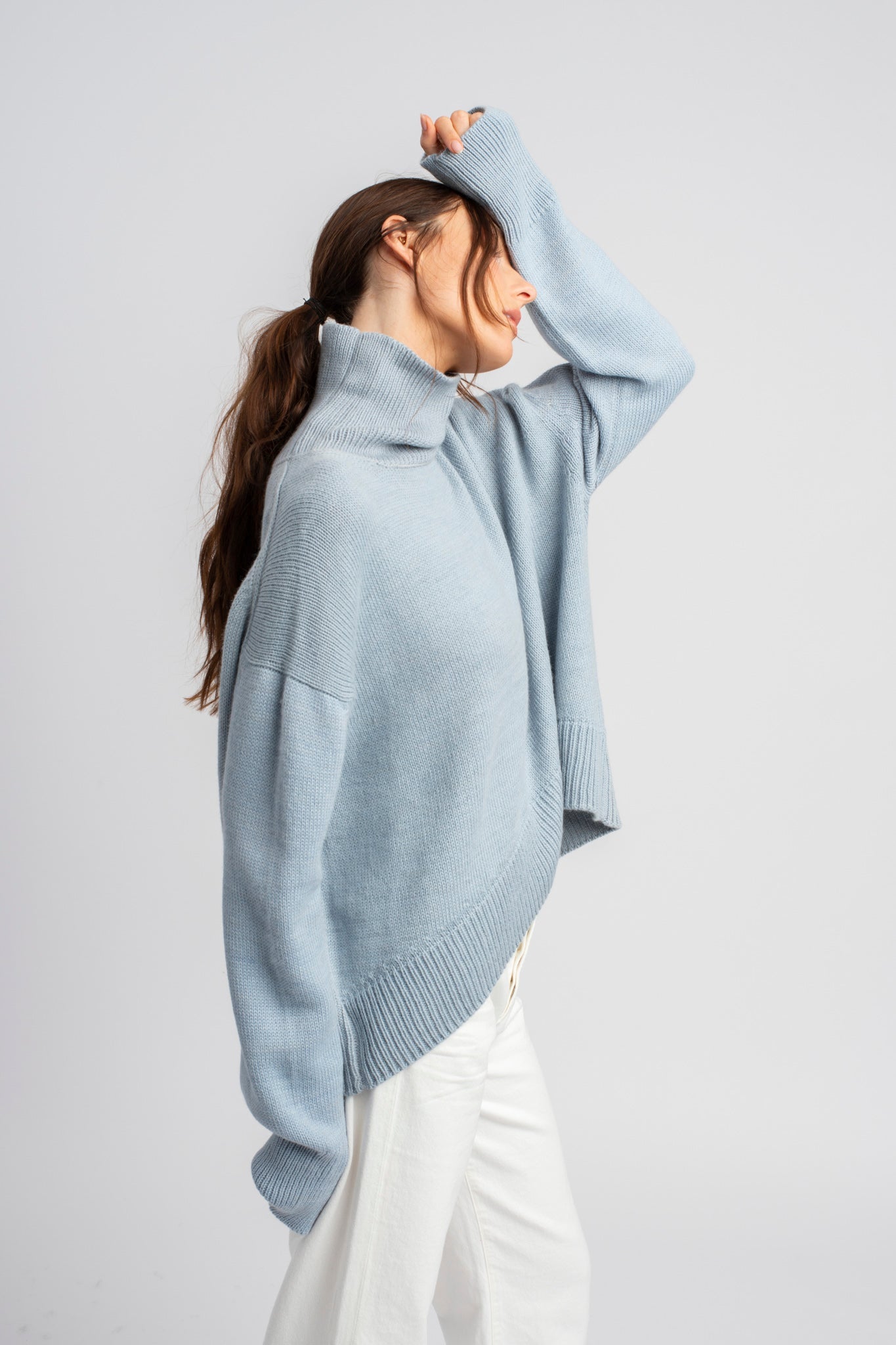 Model wearing turtleneck oversized sweater in blue alpaca wool, side standing