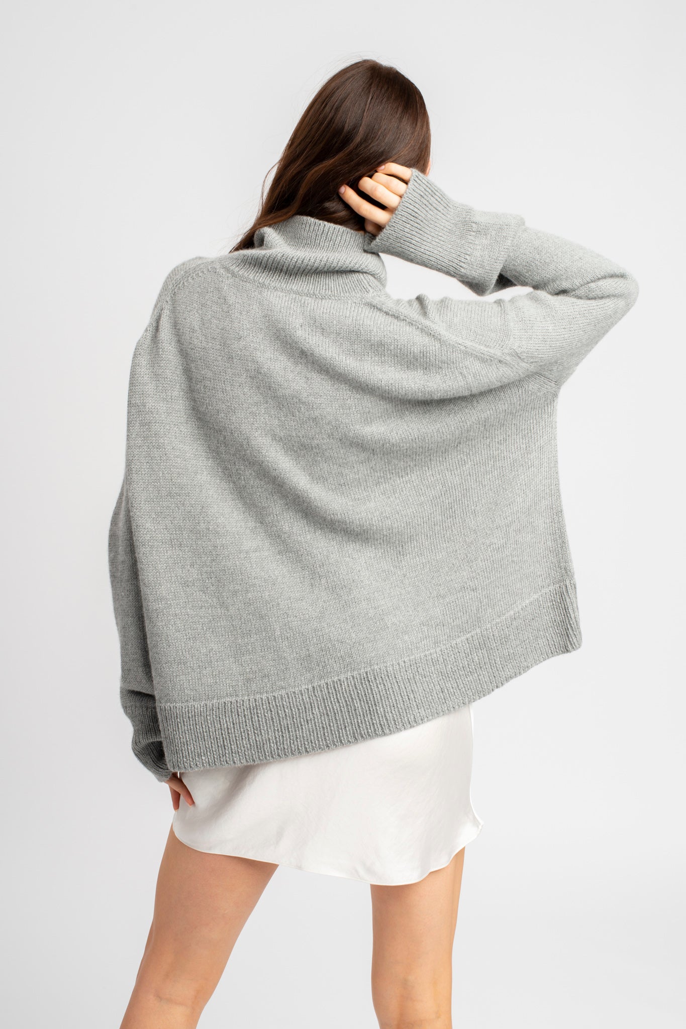 Model wearing turtleneck oversized sweater in light grey alpaca wool, back