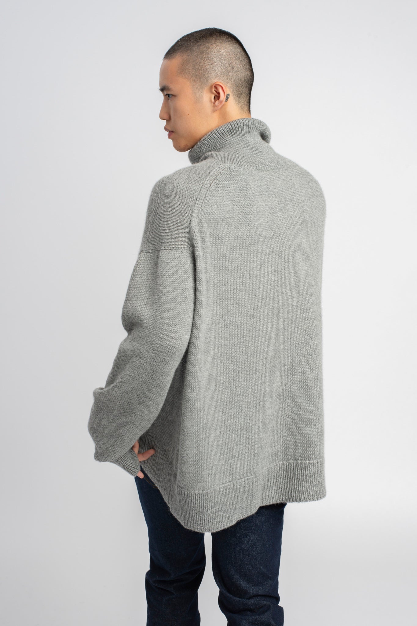 Model wearing turtleneck oversized sweater in light grey alpaca wool, back
