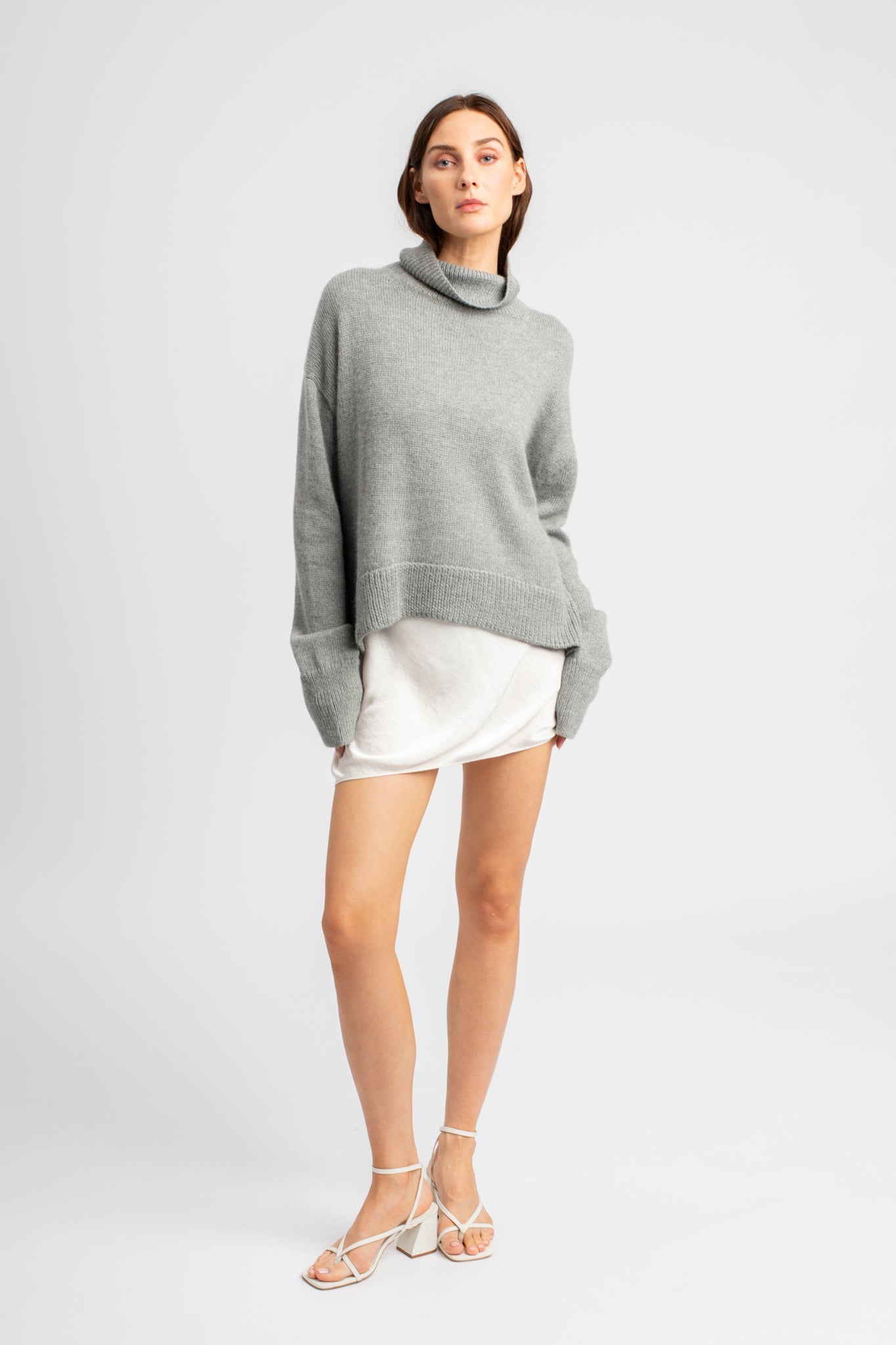Model wearing turtleneck oversized sweater in light grey alpaca wool, standing