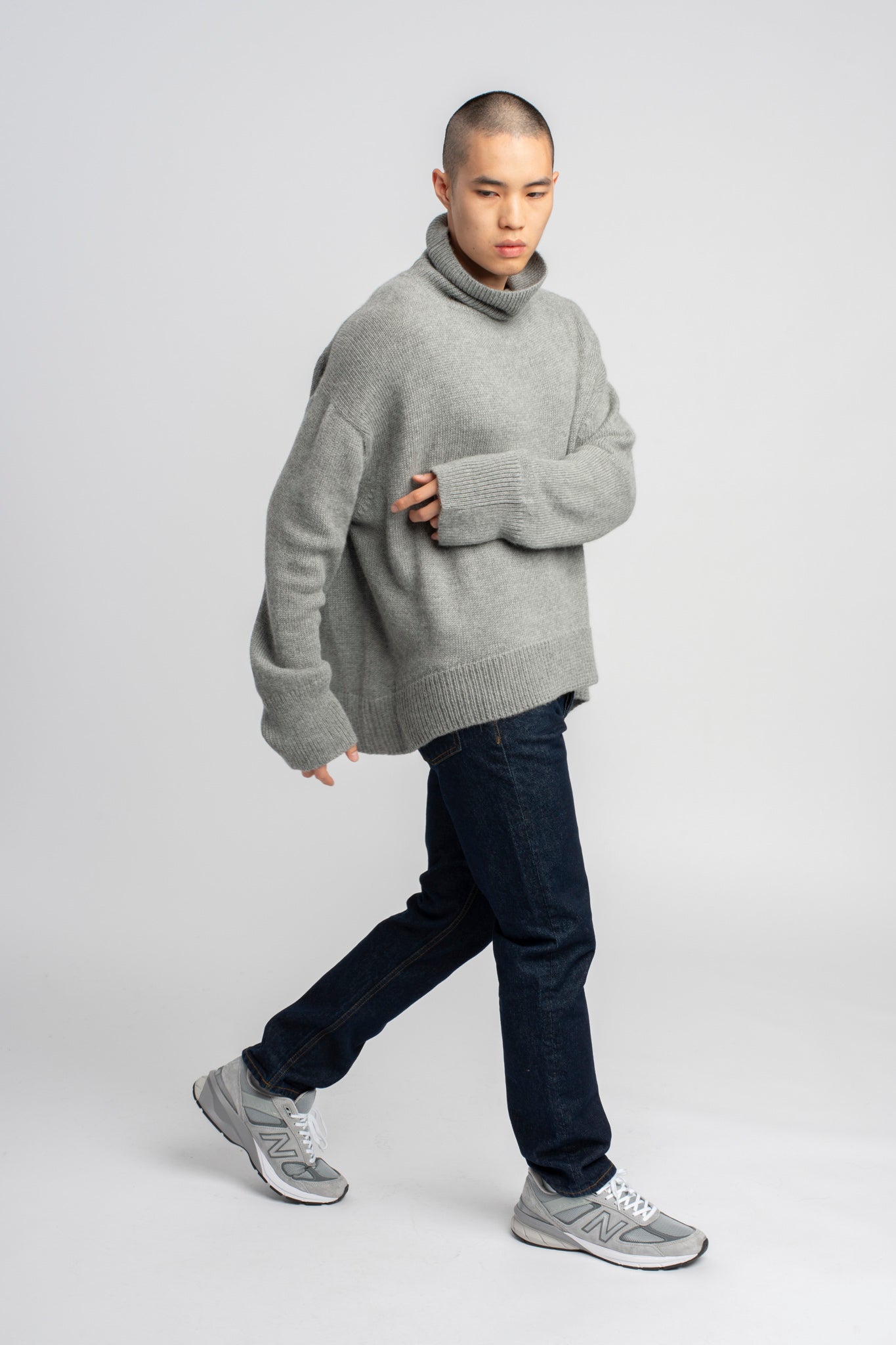 Model wearing turtleneck oversized sweater in light grey alpaca wool, walking side