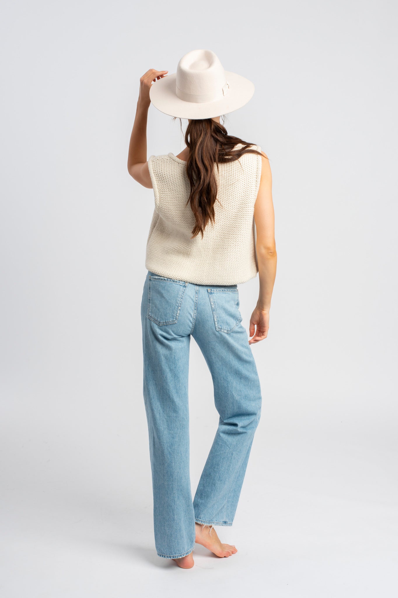 Model wearing white sweater knit vest in alpaca wool, standing outside, back