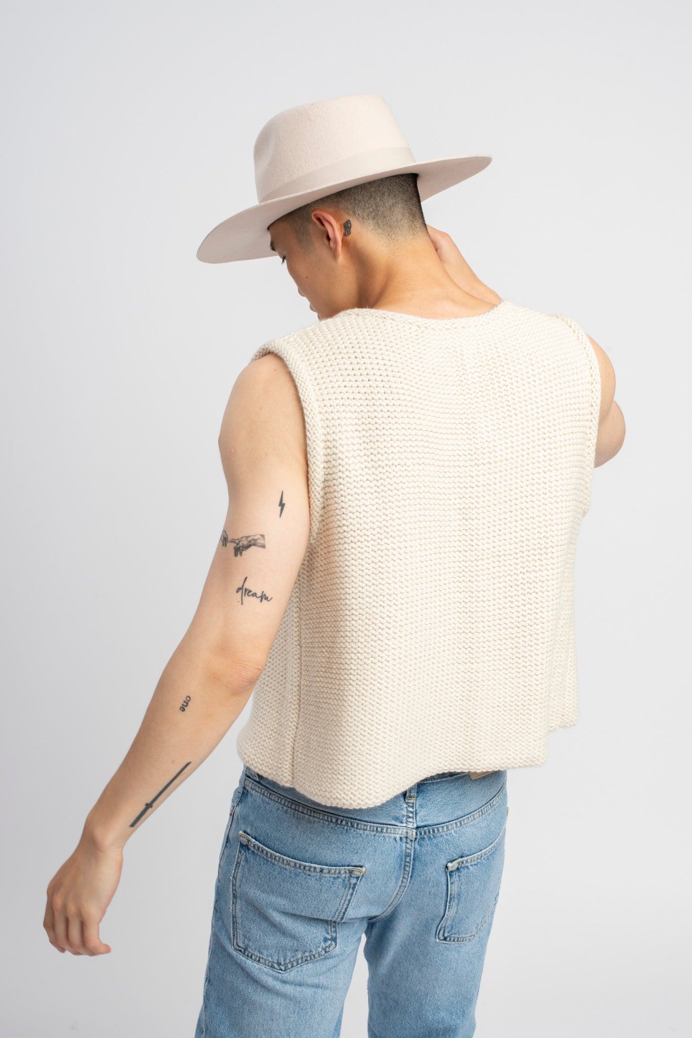 Model wearing white sweater knit vest in alpaca wool, standing outside, back close-up