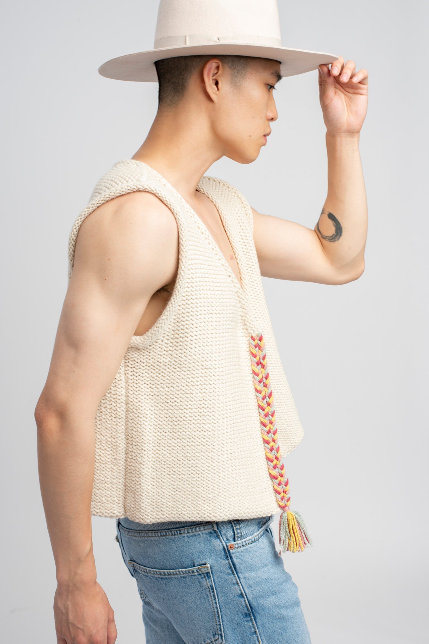 Model wearing white sweater knit vest in alpaca wool, standing outside, side