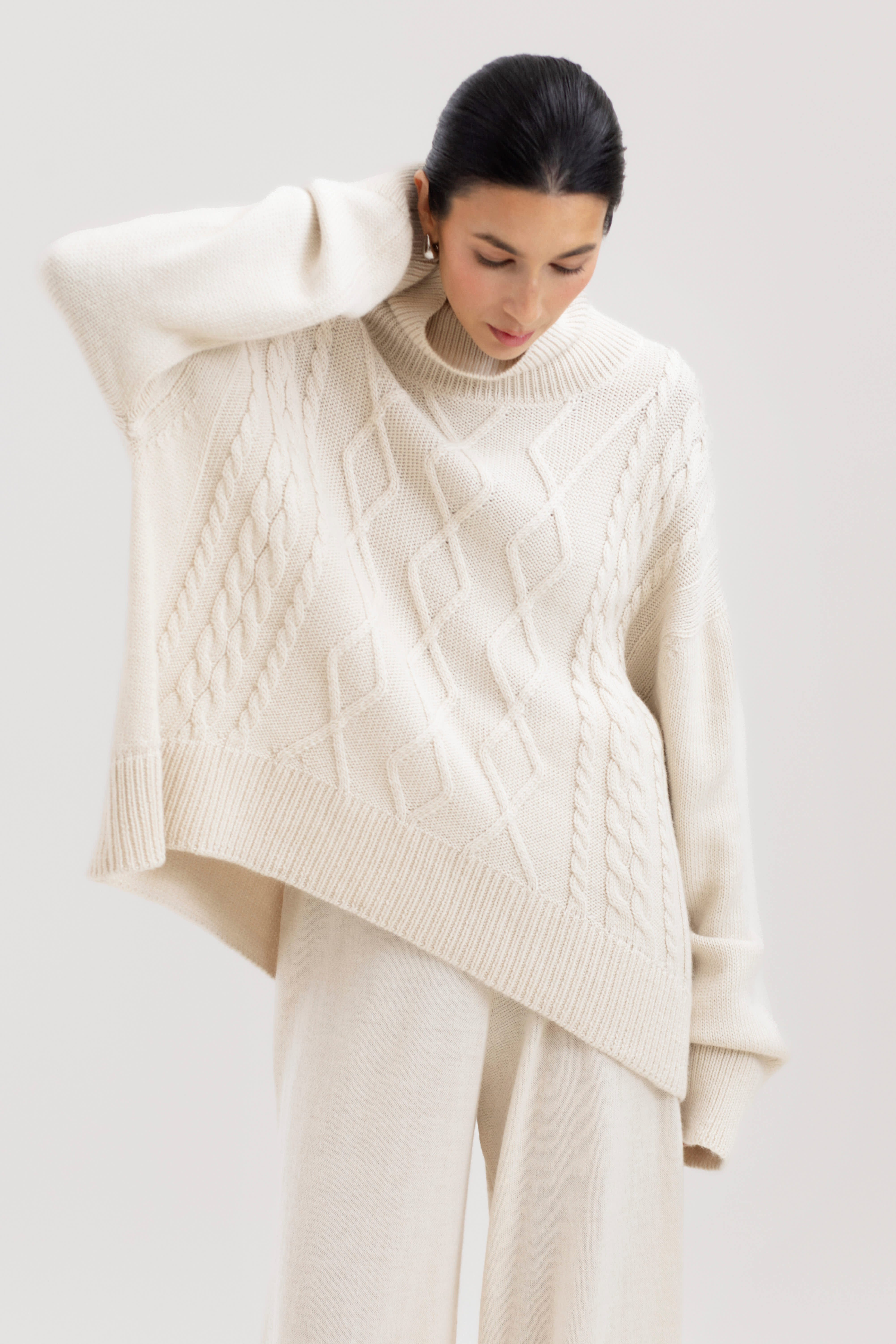 Woman wearing a cream cable knit sweater against a white background