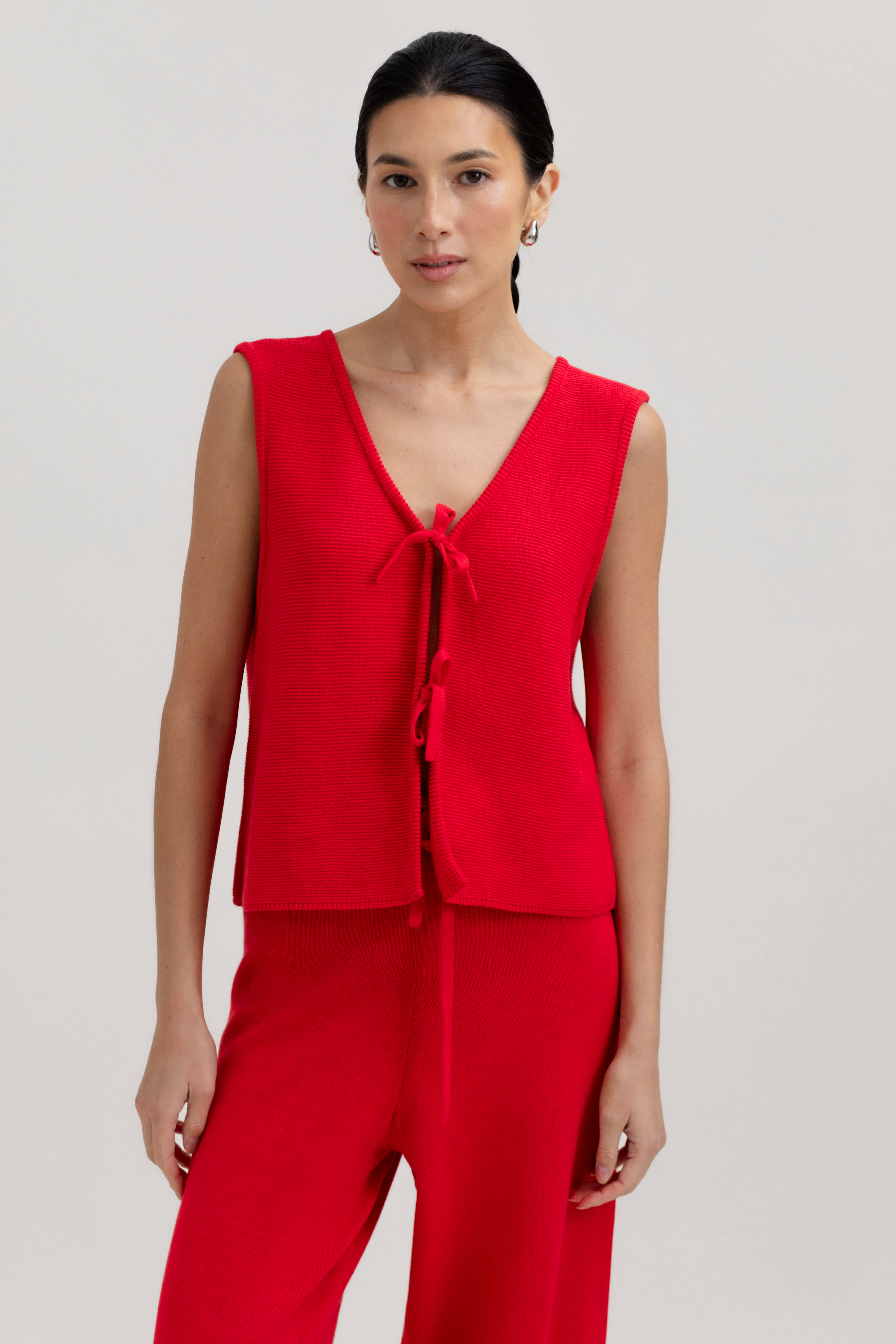 Woman wearing a red sleeveless top and pants on a plain background
