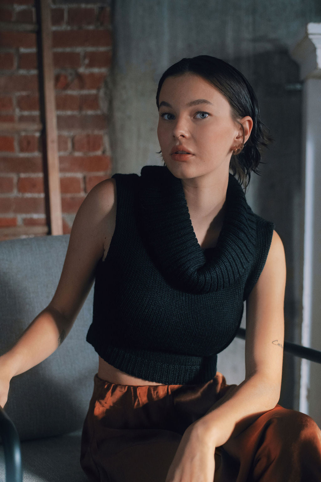 Model wearing black sweater knit crop top in alpaca wool, sitting on chair