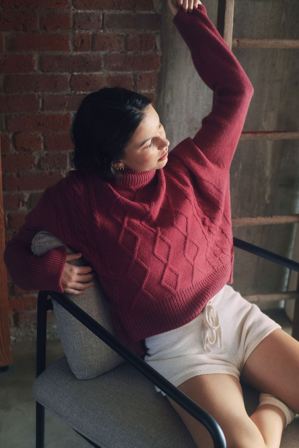 Model wearing oversized cable knit sweater in hot pink alpaca wool, sitting