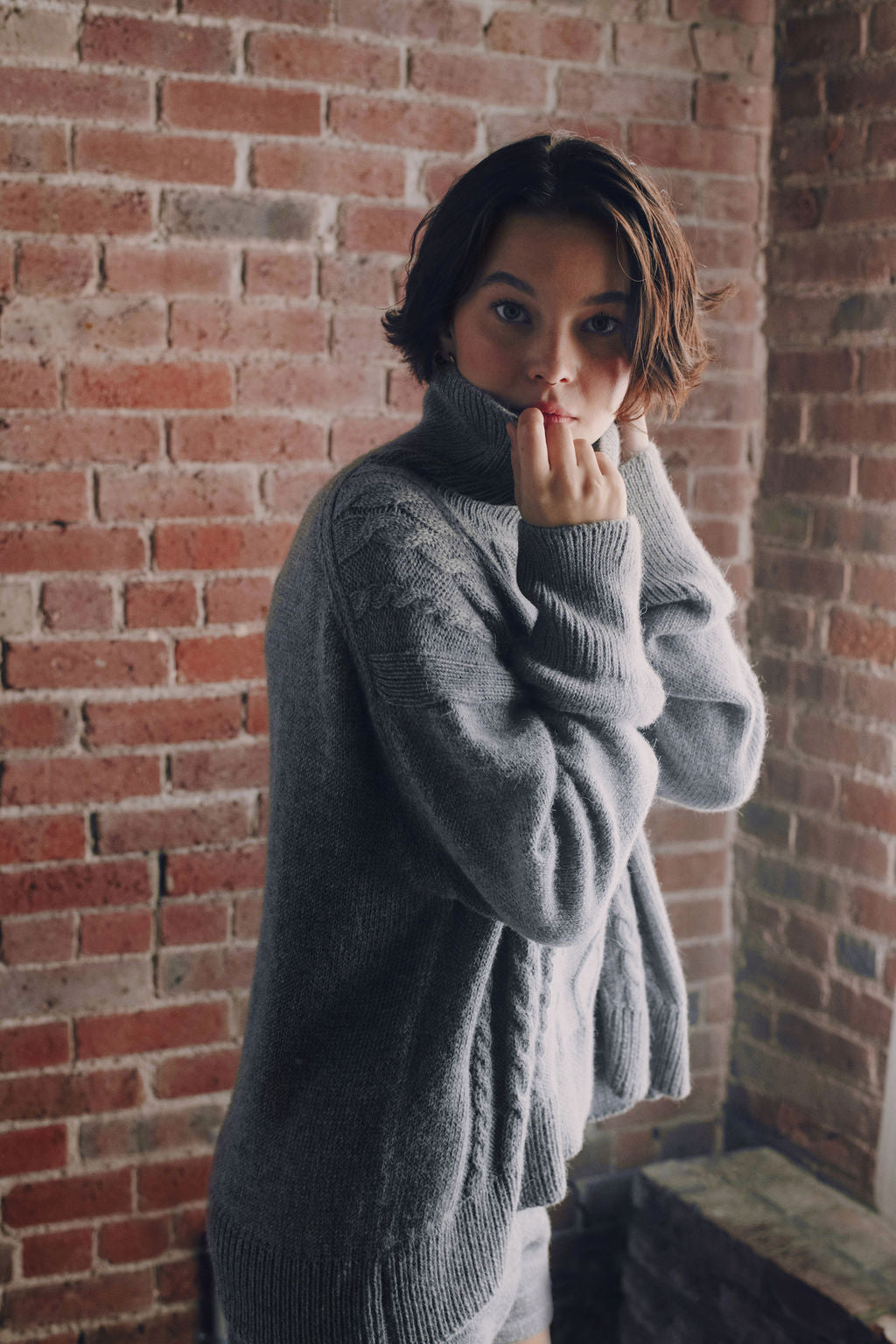 Model wearing oversized cable sweater in light grey alpaca wool, side