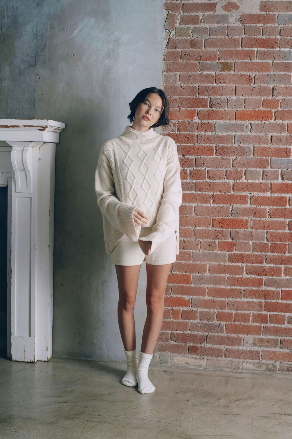 Model wearing oversized cable sweater in white alpaca wool, standing front