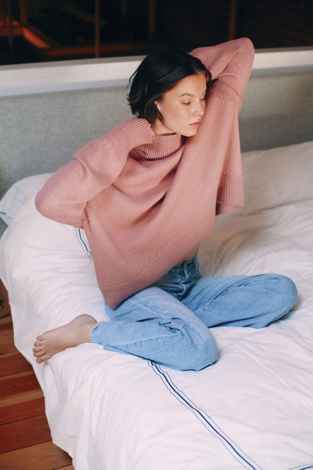 Model wearing oversized sweater in light pink alpaca wool, sitting pose