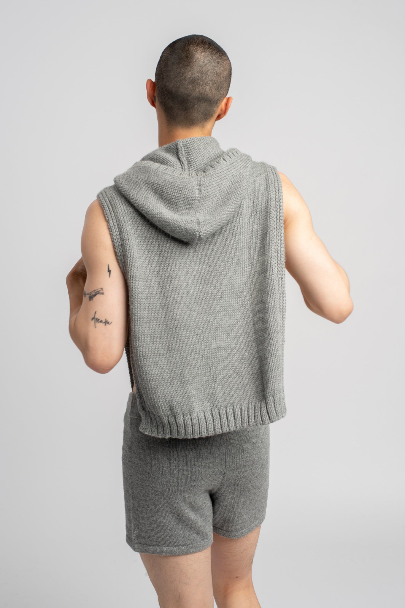 Model wearing poncho in light grey alpaca wool, standing back view of hood