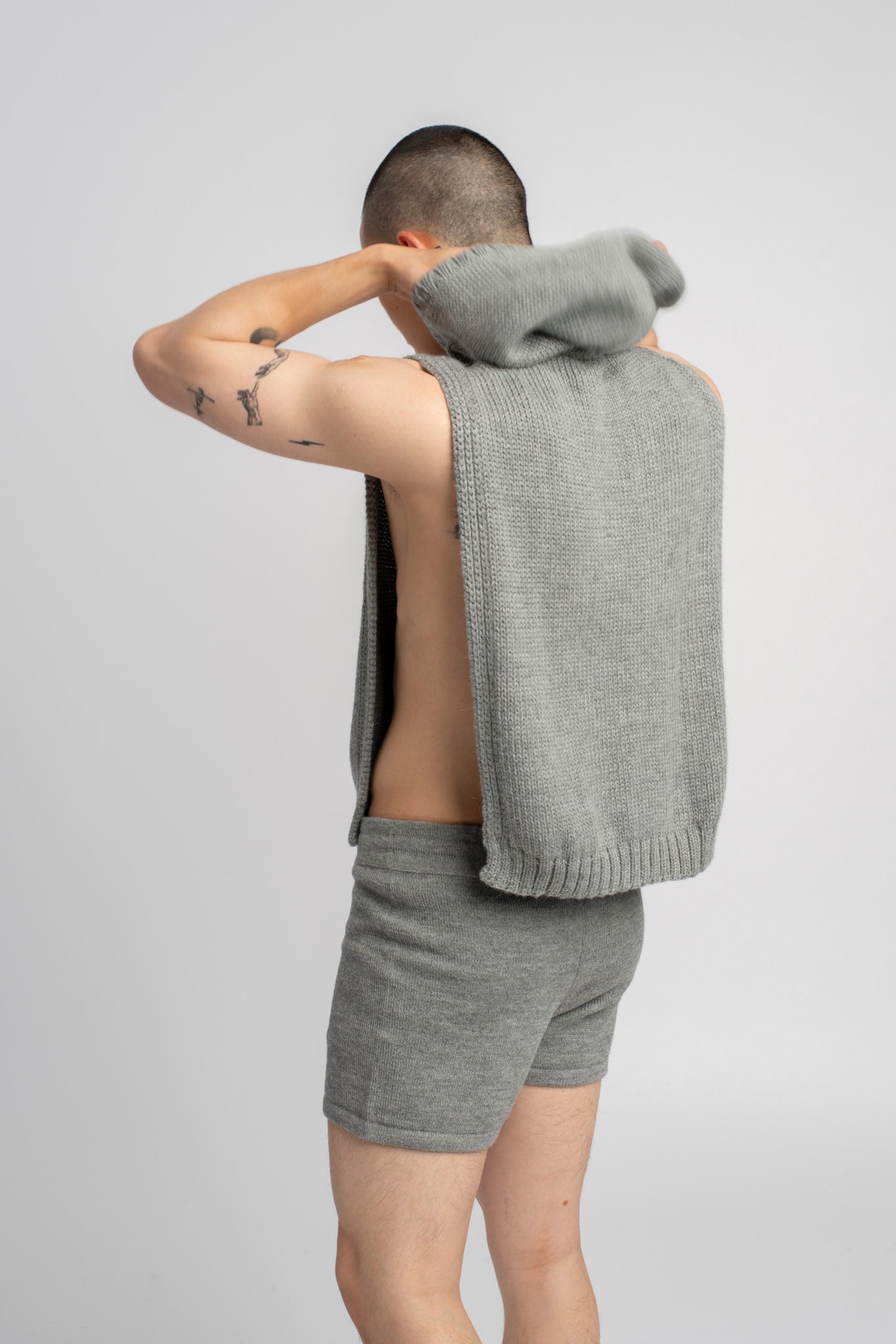 Model wearing poncho in light grey alpaca wool, putting on hood