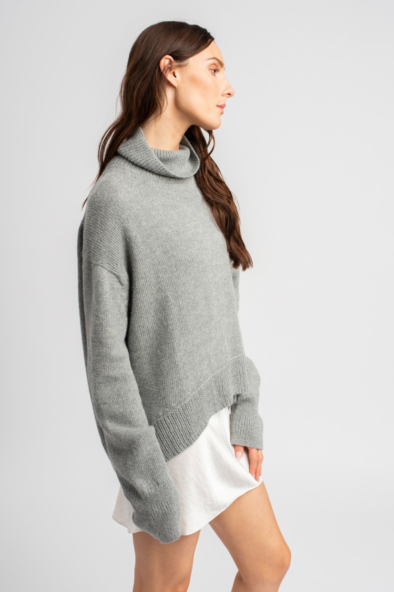 Model wearing turtleneck oversized sweater in light grey alpaca wool, standing side