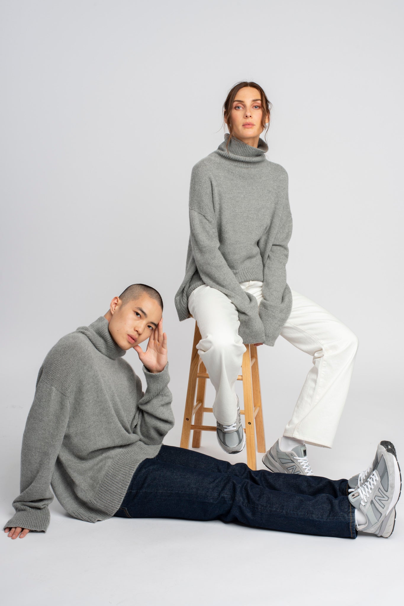 Models wearing turtleneck oversized sweater in light grey alpaca wool, sitting down