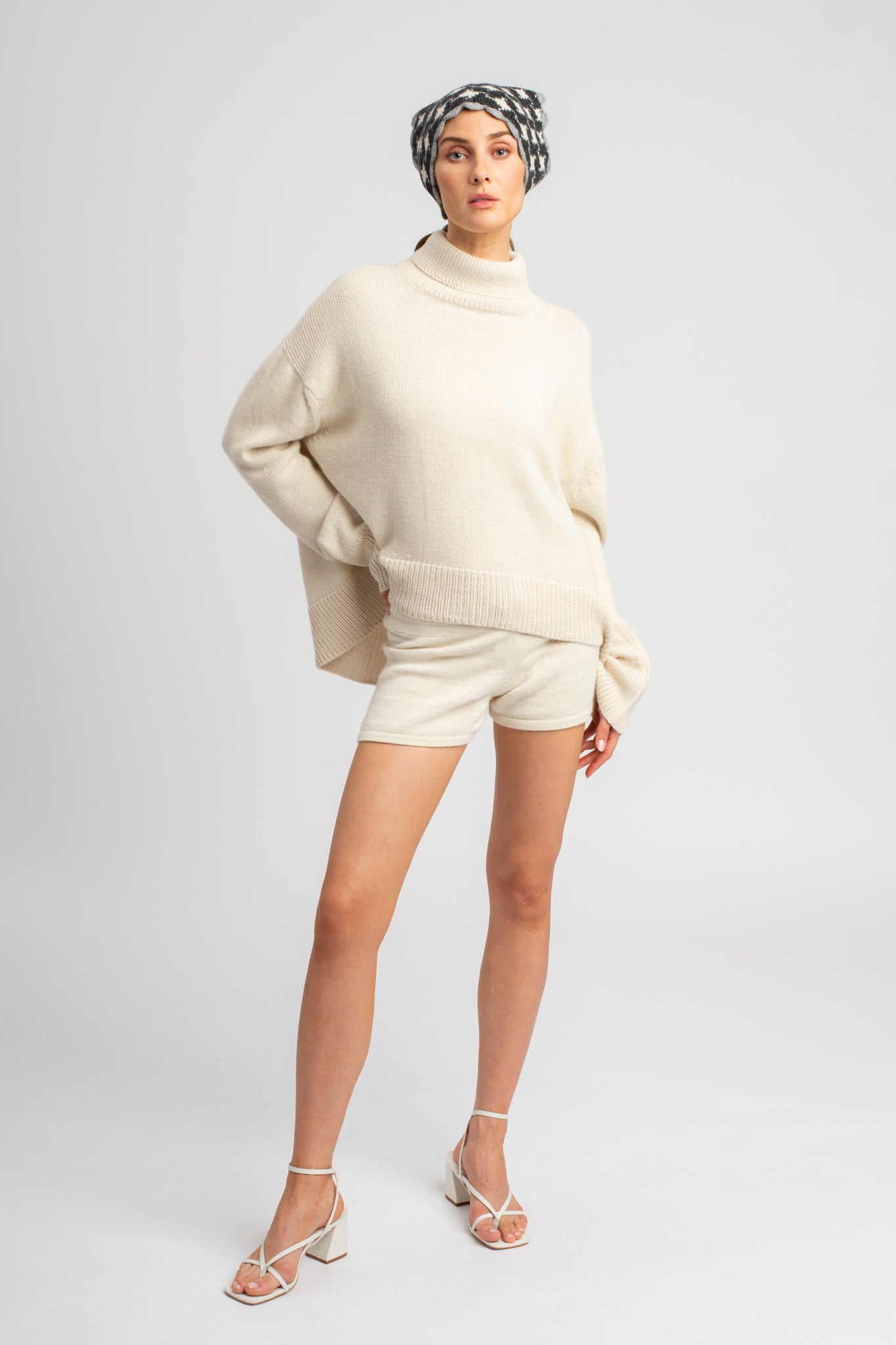 Model wearing turtleneck oversized sweater in white alpaca wool with headscarf, front standing